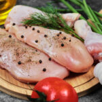 Raw chicken fillet and legs on wooden plate with fresh vegetables